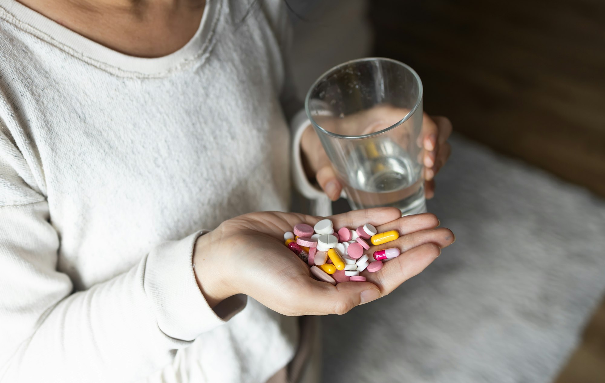 Asian woman in one hand handful of tablets, in other glass of clean water close up. Lot of pills. la
